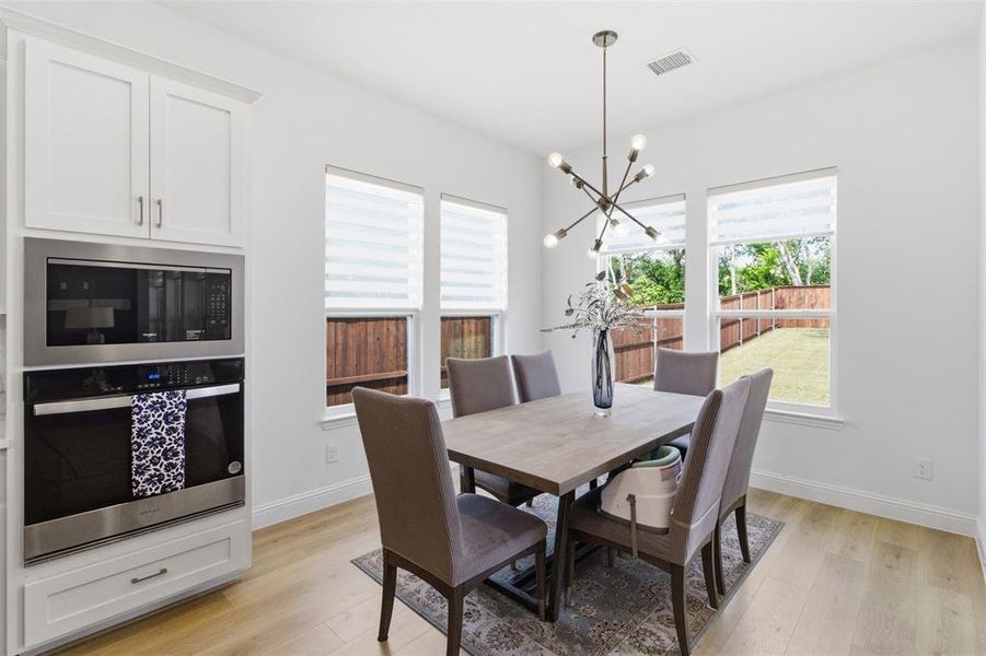 Bright dining area featuring wood-finish flooring, white walls, and multiple windows with horizontal blinds
