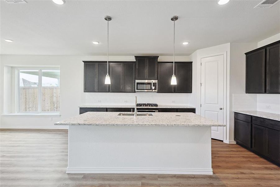 Kitchen featuring light stone counters, sink, wood-type flooring, and a kitchen island with sink