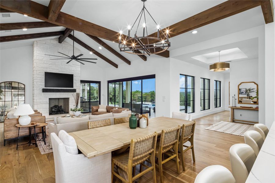 Dining area featuring beam ceiling, high vaulted ceiling, light hardwood / wood-style flooring, ceiling fan, and a fireplace