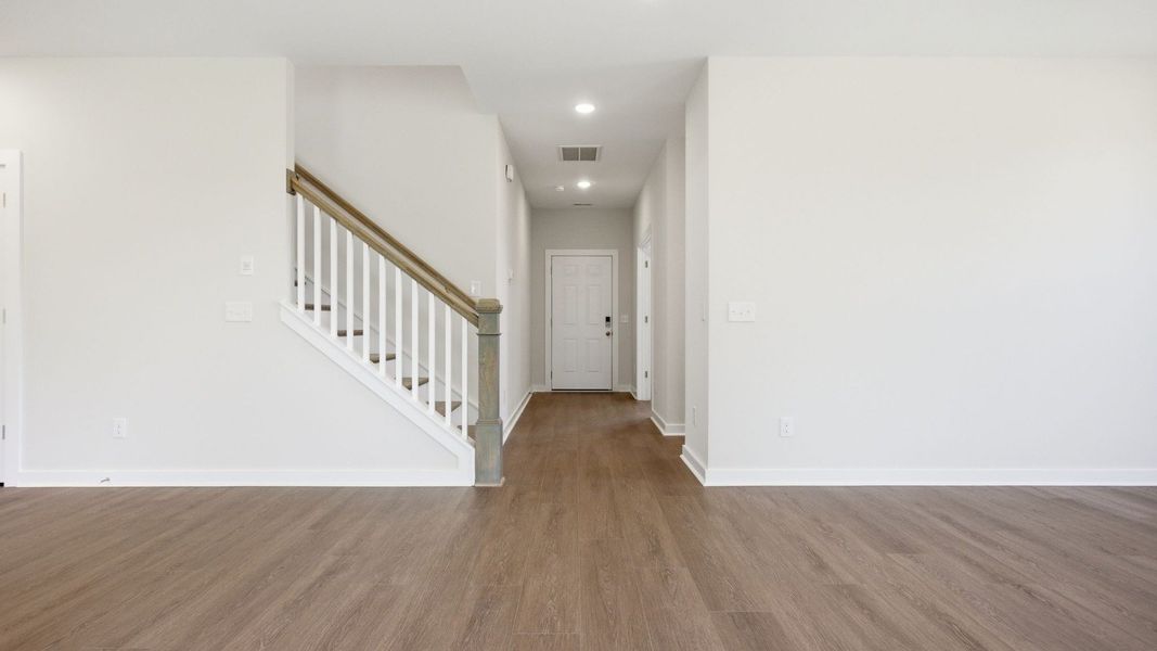 Hallway to entry door with hard surface flooring and view of staircase Hallway to entry door with hard surface flooring and view of staircase
