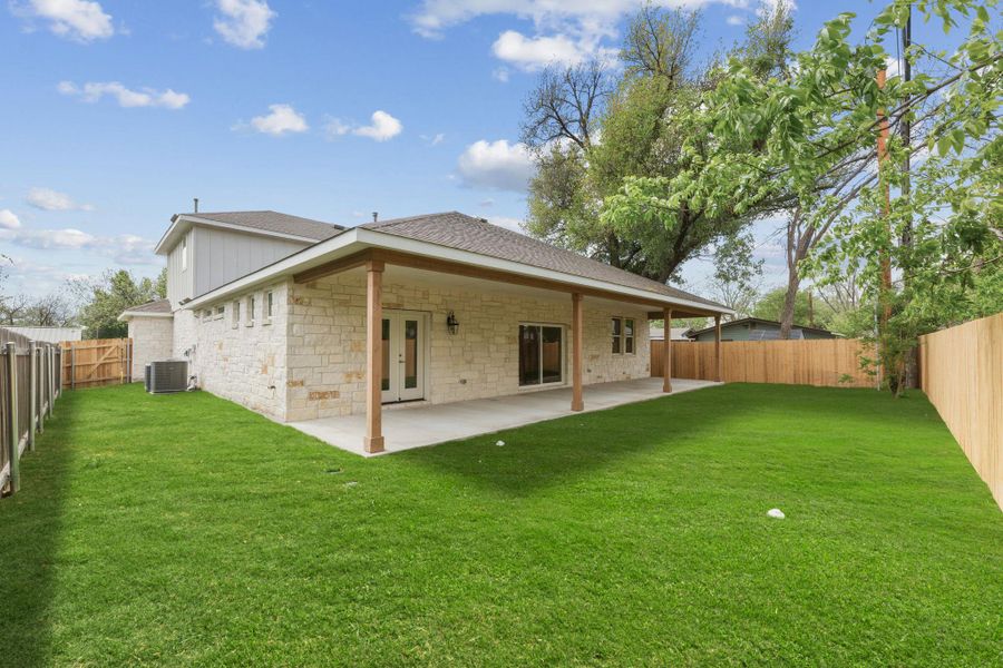 Back of property with a privacy fence, a large covered patio with ceiling fans and nice ambient lighting, french doors to both the primary and living room spaces, and beautiful stone siding
