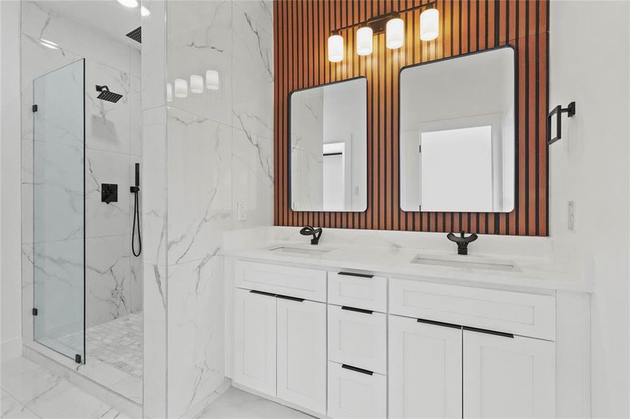 Bathroom with double vanity, a marble finish shower, and light marble finish floors