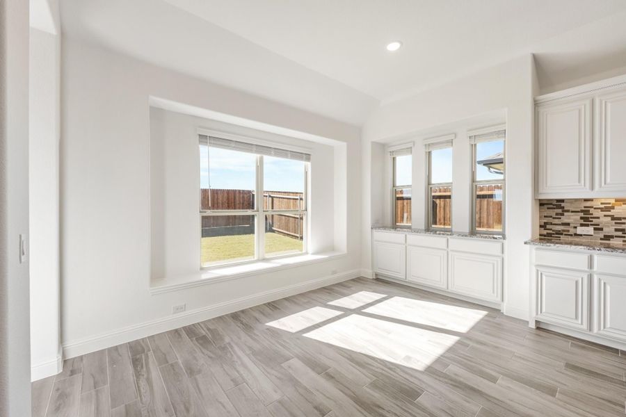 Bright dining area with wood-look tile floors, large windows, and white kitchen cabinets with tile backsplash nearby. Bright dining area with wood-look tile floors, large windows, and white kitchen cabinets with tile backsplash nearby.