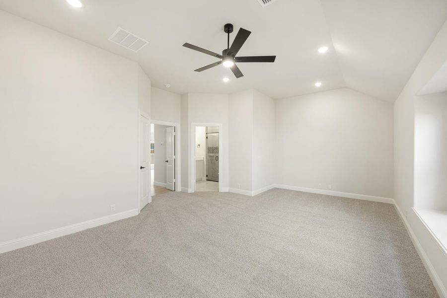 Empty bedroom with vaulted ceiling, ceiling fan, carpet flooring, and ensuite bathroom doorway