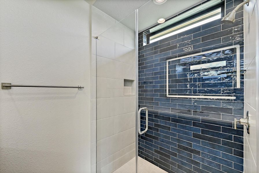 A glass-enclosed shower boasts sleek subway tiling and a convenient recessed shelf.