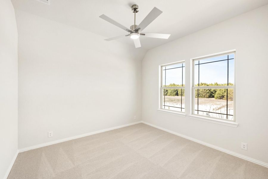 Empty bedroom with vaulted ceiling, ceiling fan, carpet flooring, and two windows with outdoor views Empty bedroom with vaulted ceiling, ceiling fan, carpet flooring, and two windows with outdoor views