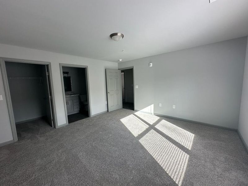 Unfurnished bedroom featuring a walk in closet, connected bathroom, a closet, and carpet flooring