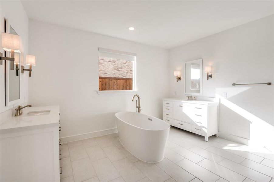 Beautiful primary bathroom featuring a soaking tub, two vanities, recessed lighting, and light tile patterned flooring Beautiful primary bathroom featuring a soaking tub, two vanities, recessed lighting, and light tile patterned flooring