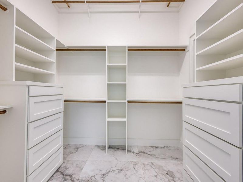 Spacious custom closet featuring light marble finish floors, build in shelves and drawers