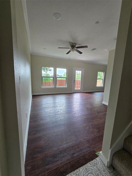 Unfurnished room featuring ornamental molding, a ceiling fan, dark wood-style floors, baseboards, and stairway