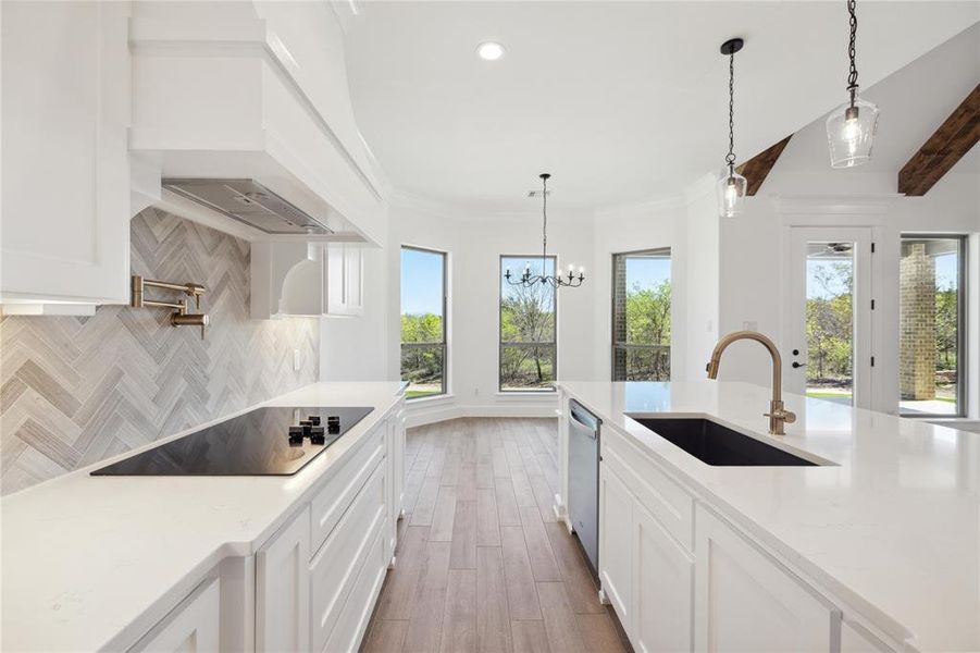 Kitchen with white cabinets, backsplash, electric stovetop, decorative light fixtures, and sink