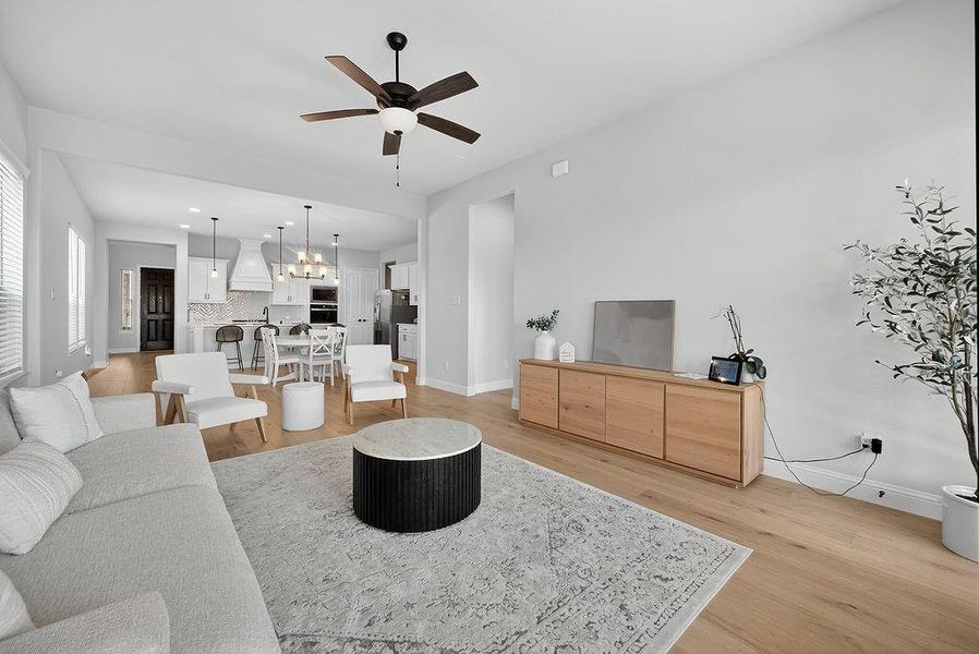 Spacious open-concept living area featuring light wood-finish flooring, a contemporary ceiling fan, and recessed lighting