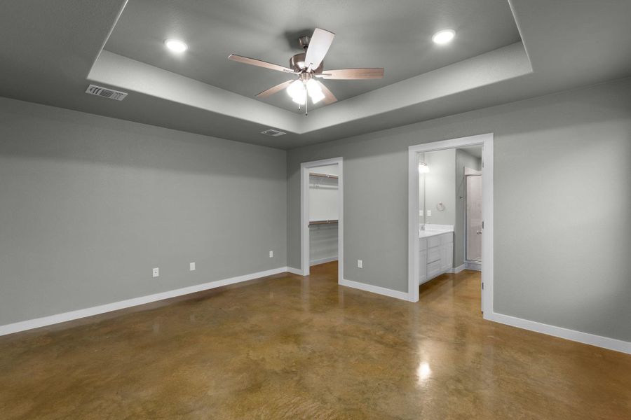 Modern primary bedroom featuring polished concrete floors and a stylish tray ceiling with recessed lighting.