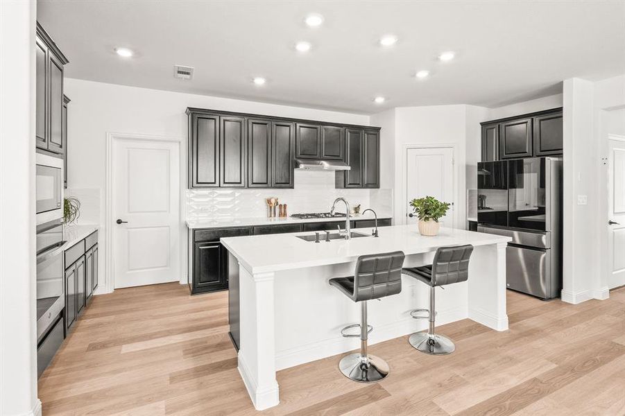 Kitchen featuring stainless steel appliances, an island with sink, a breakfast bar area, recessed lighting, and light wood-style flooring