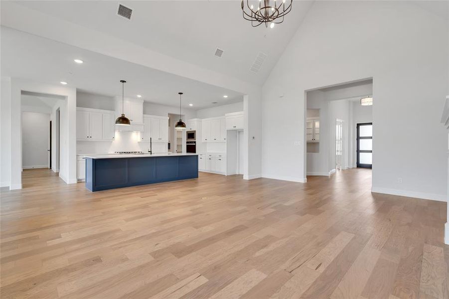 Unfurnished living room with high vaulted ceiling, light hardwood / wood-style floors, and a notable chandelier