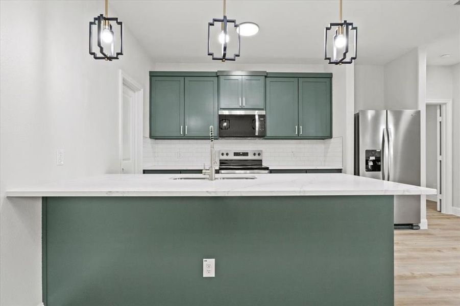 Kitchen featuring light stone counters, pendant lighting, and appliances with stainless steel finishes