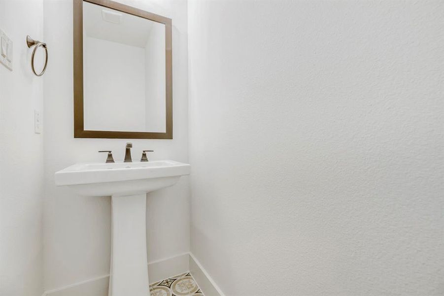 Pedestal sink with dark-toned fixtures and a coordinating framed mirror