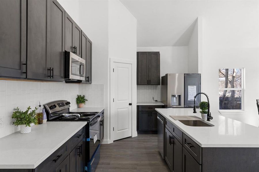 Kitchen featuring tasteful backsplash, stainless steel appliances, a kitchen island with sink, sink, and dark hardwood / wood-style floors