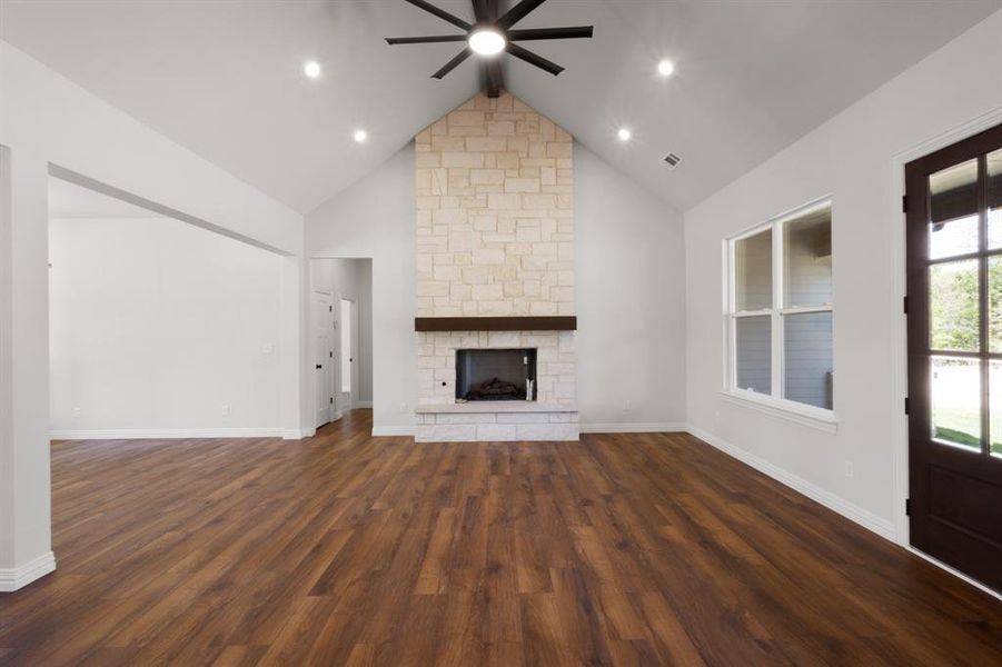 Unfurnished living room featuring high vaulted ceiling, a fireplace, dark wood-type flooring, a ceiling fan, and visible vents