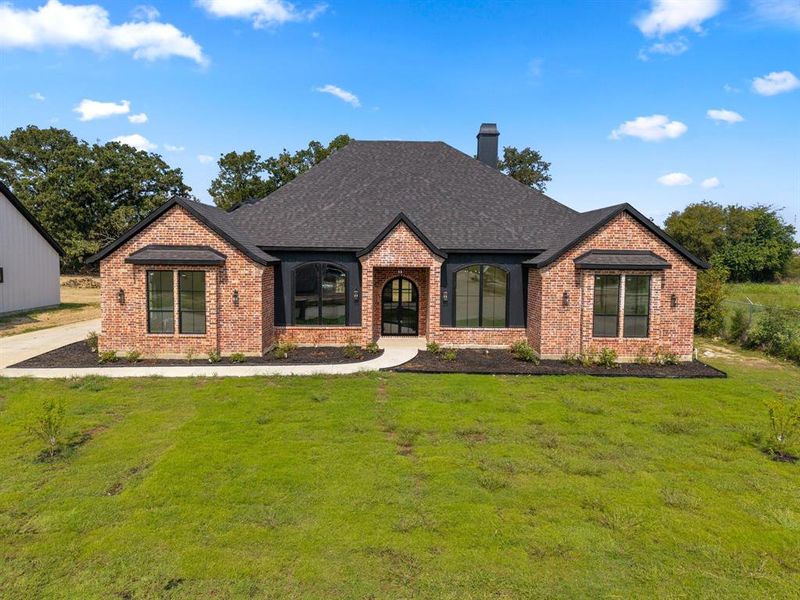 French provincial home with a front lawn, brick siding, roof with shingles, and a chimney