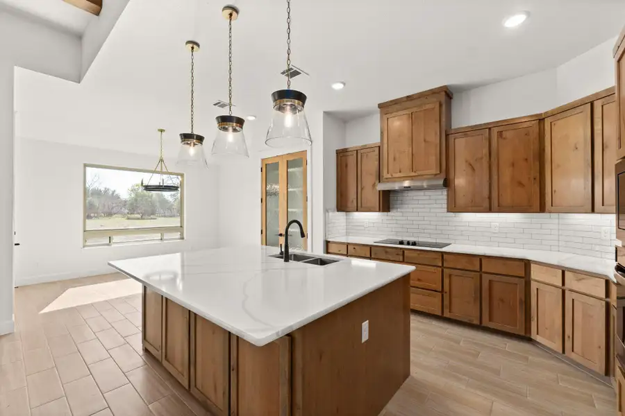 Kitchen with brown cabinetry, decorative backsplash, decorative light fixtures, an island with sink, and recessed lighting