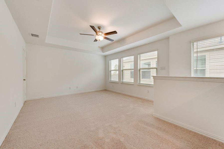 Empty room with a tray ceiling, light carpet, and ceiling fan