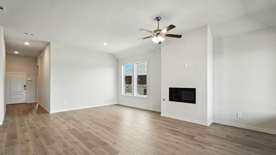 Spacious living area featuring wood-finish flooring, an integrated electric fireplace, and abundant natural light from multiple windows Spacious living area featuring wood-finish flooring, an integrated electric fireplace, and abundant natural light from multiple windows