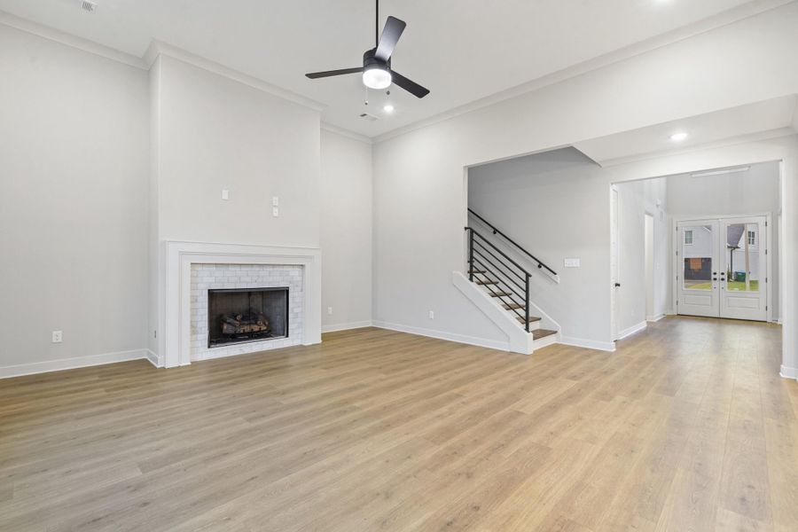 Spacious interior featuring high ceilings, light wood-finish flooring, a contemporary fireplace with a tiled surround, a ceiling fan, and a staircase with a modern black railing Spacious interior featuring high ceilings, light wood-finish flooring, a contemporary fireplace with a tiled surround, a ceiling fan, and a staircase with a modern black railing