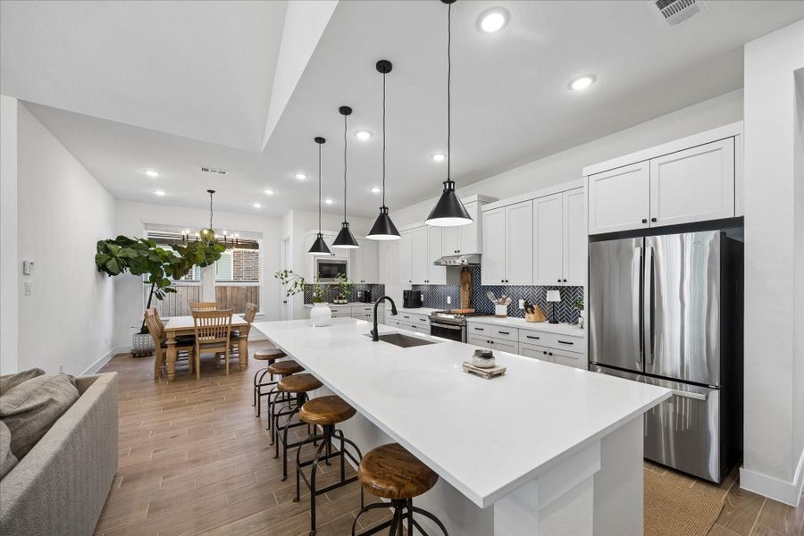 Expansive quartz island offering abundant seating and workspace, perfectly complemented by custom cabinetry and high-end stainless steel appliances. The open layout highlights the seamless flow between the kitchen, dining, and living areas, all unified by beautiful wood-plank-look tile flooring. Expansive quartz island offering abundant seating and workspace, perfectly complemented by custom cabinetry and high-end stainless steel appliances. The open layout highlights the seamless flow between the kitchen, dining, and living areas, all unified by beautiful wood-plank-look tile flooring.