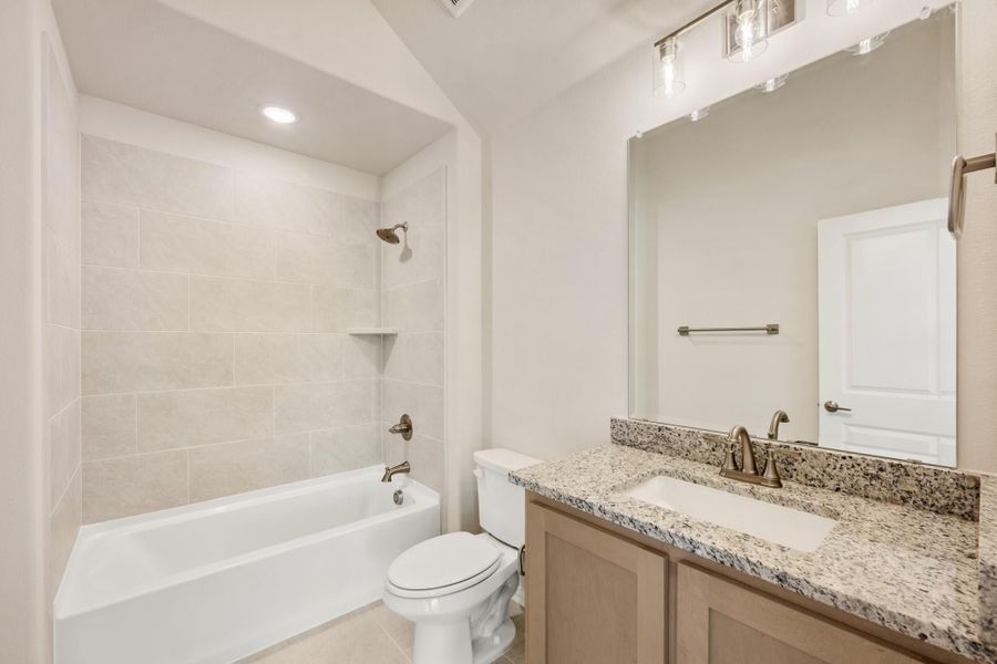 Bathroom with tiled tub-shower combo, granite vanity countertop, and large mirror with light fixture above Bathroom with tiled tub-shower combo, granite vanity countertop, and large mirror with light fixture above