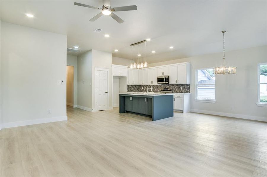 Kitchen featuring tasteful backsplash, white cabinets, ceiling fan with notable chandelier, open floor plan, and stainless steel appliances