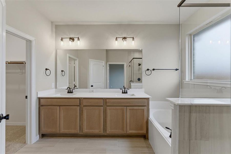 Bathroom featuring a double vanity with light wood-finish cabinetry, white countertops, and black hardware