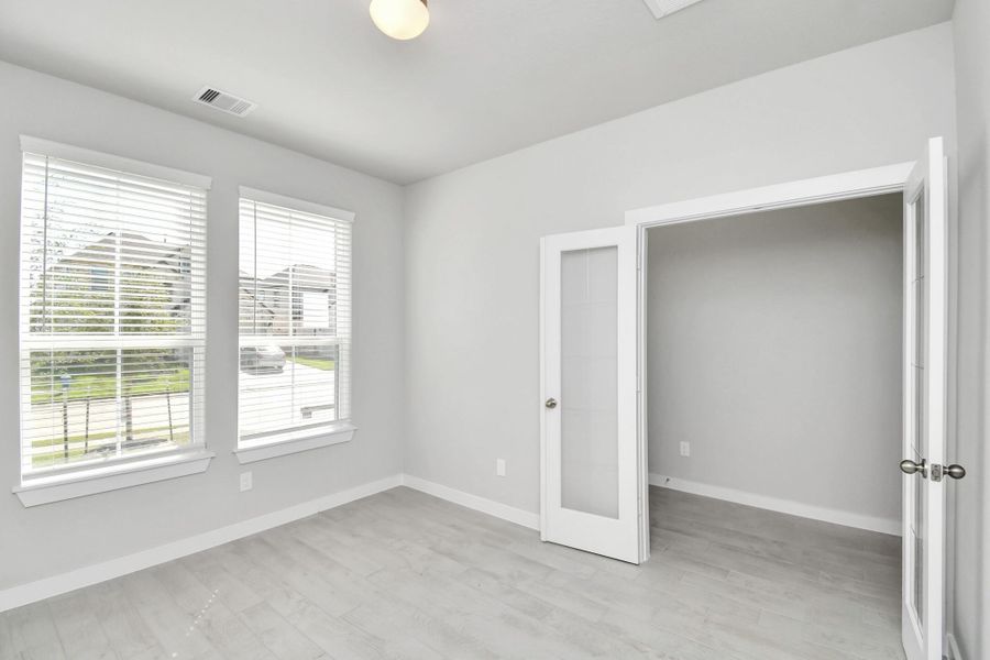 Experience the perfect blend of sophistication and warmth in this home office, boasting elegant wood-look tile flooring and flooded with natural light from expansive windows and French doors. Sample photo of completed home with similar floor plan. Actual colors and selections may vary.