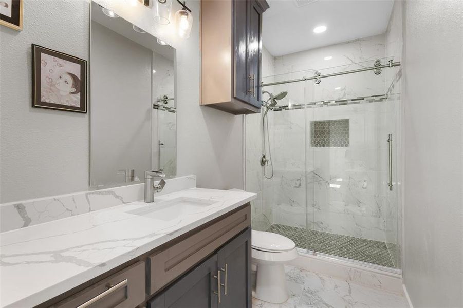 Bathroom featuring vanity, a marble finish shower, light marble finish flooring, and a textured wall