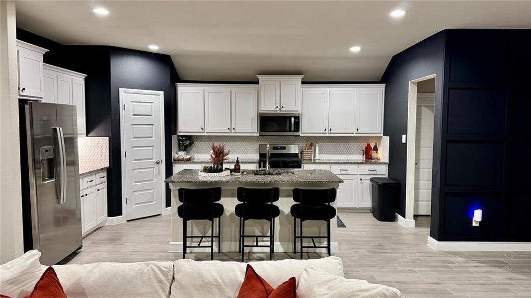 Open-concept kitchen featuring white cabinetry, a built-in microwave, and a hexagonal tile backsplash
