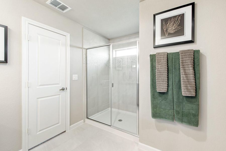 Bathroom with glass-door walk-in shower, white tile floors, and green towels on wall rack Bathroom with glass-door walk-in shower, white tile floors, and green towels on wall rack