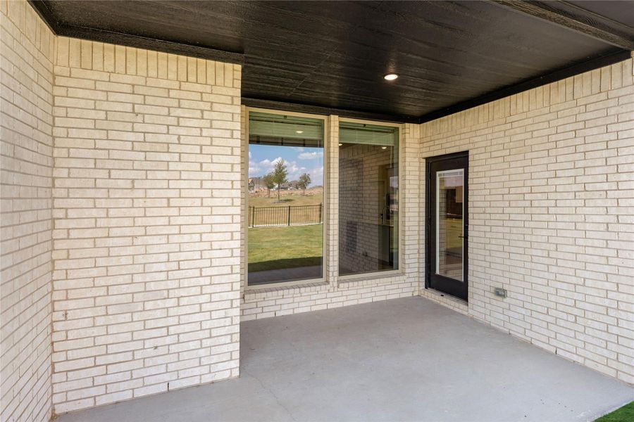 Covered back patio with concrete floor, white brick walls, sliding glass door, and dark wood ceiling