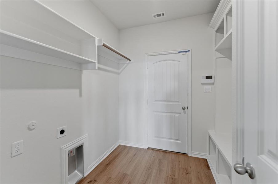 Laundry area featuring built-in shelving, hanging rod, wood-finish flooring, and a utility sink hookup