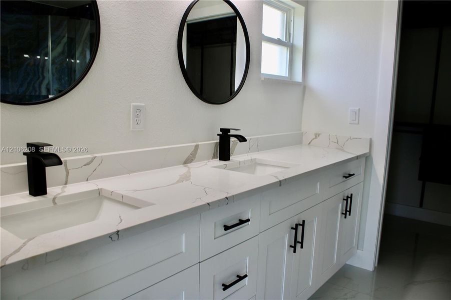 Dual-vanity cabinet featuring white shaker-style doors, matte black hardware, stone-patterned countertops, undermount sinks, and circular wall-mounted mirrors with matte black frames