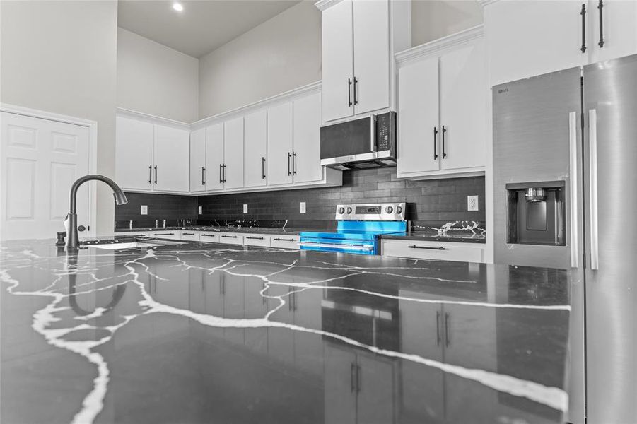 Kitchen with appliances with stainless steel finishes, decorative backsplash, white cabinets, dark stone countertops, and a towering ceiling