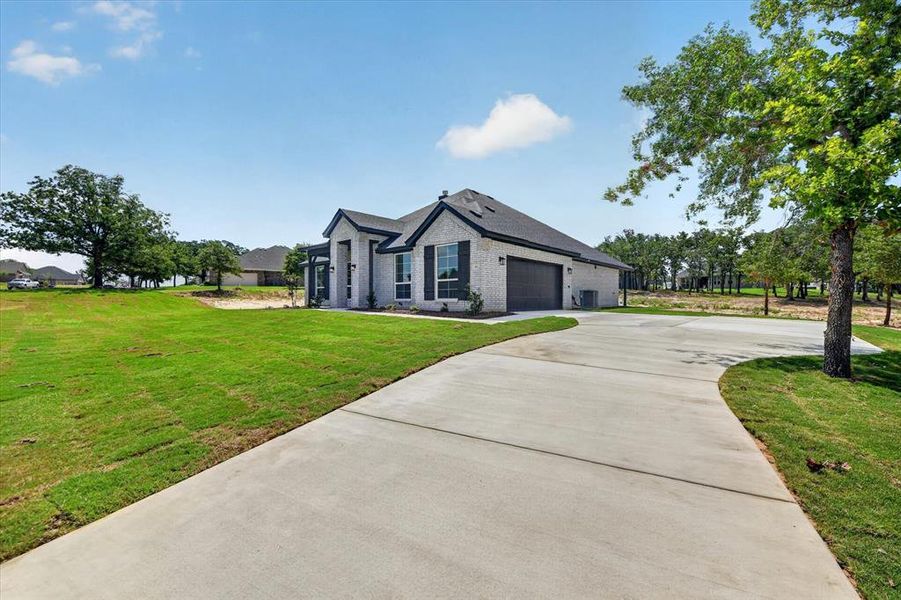 Contemporary-style home featuring a light-colored brick exterior, dark-trimmed windows with shutters, and a dark shingle roof Contemporary-style home featuring a light-colored brick exterior, dark-trimmed windows with shutters, and a dark shingle roof