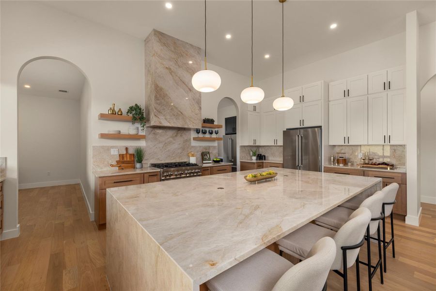 Kitchen with arched walkways, open shelves, backsplash, light stone counters, and a high ceiling