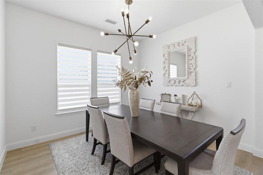 Dining area featuring an open-concept layout, modern sputnik chandelier, two large windows with blinds, light wood-finish flooring, and white baseboards