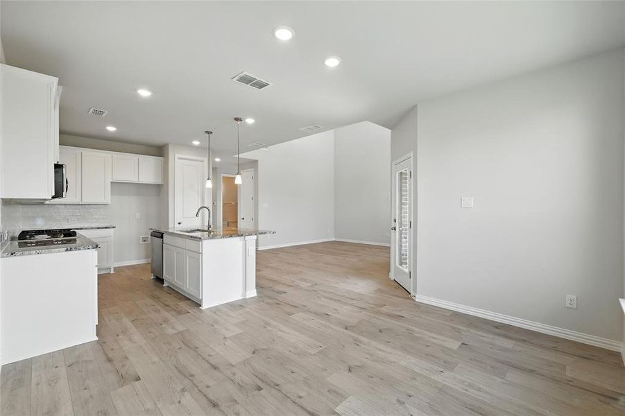 Kitchen with dark stone countertops, a kitchen island with sink, white cabinetry, light wood-type flooring, and recessed lighting Kitchen with dark stone countertops, a kitchen island with sink, white cabinetry, light wood-type flooring, and recessed lighting