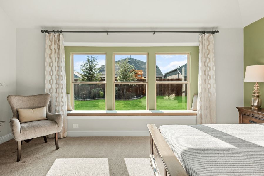 Bedroom with triple windows, window seat, accent chair, and backyard view