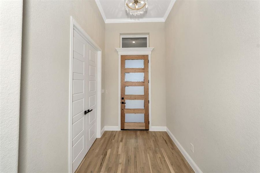 Doorway to outside with light hardwood / wood-style flooring, crown molding, and a notable chandelier