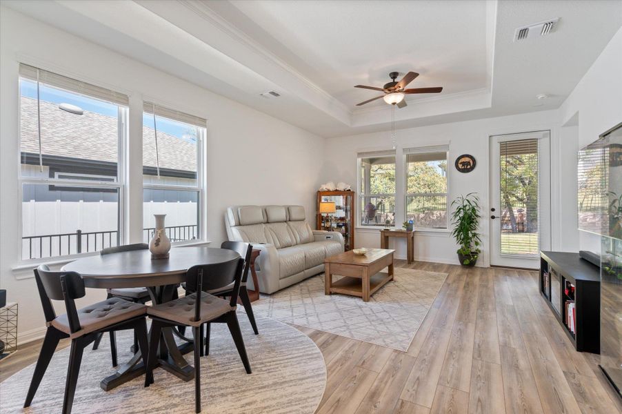 Dining area featuring a ceiling fan, light wood-style flooring, healthy amount of natural light, and a tray ceiling Dining area featuring a ceiling fan, light wood-style flooring, healthy amount of natural light, and a tray ceiling