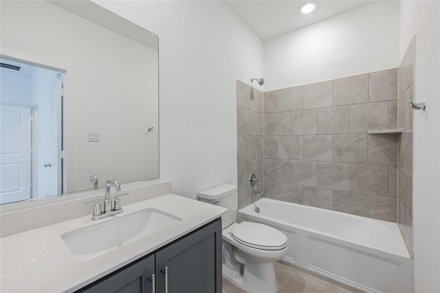 Full bathroom featuring vanity, tiled shower / bath combo, and toilet