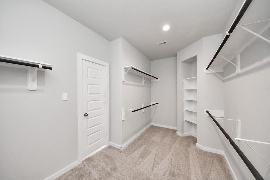 Walk-in closet that epitomizes luxury and practicality. This generously sized space features built-in shelving, offering abundant room for impeccable organization. High ceilings and recessed lighting create a bright and welcoming ambiance. Sample photo of completed home with similar floor plan. Actual colors and selections may vary.