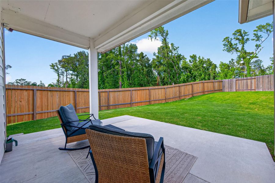 This photo showcases a covered patio with comfortable seating, overlooking a spacious, fenced backyard with lush grass and bordering trees, perfect for relaxation and privacy. This photo showcases a covered patio with comfortable seating, overlooking a spacious, fenced backyard with lush grass and bordering trees, perfect for relaxation and privacy.